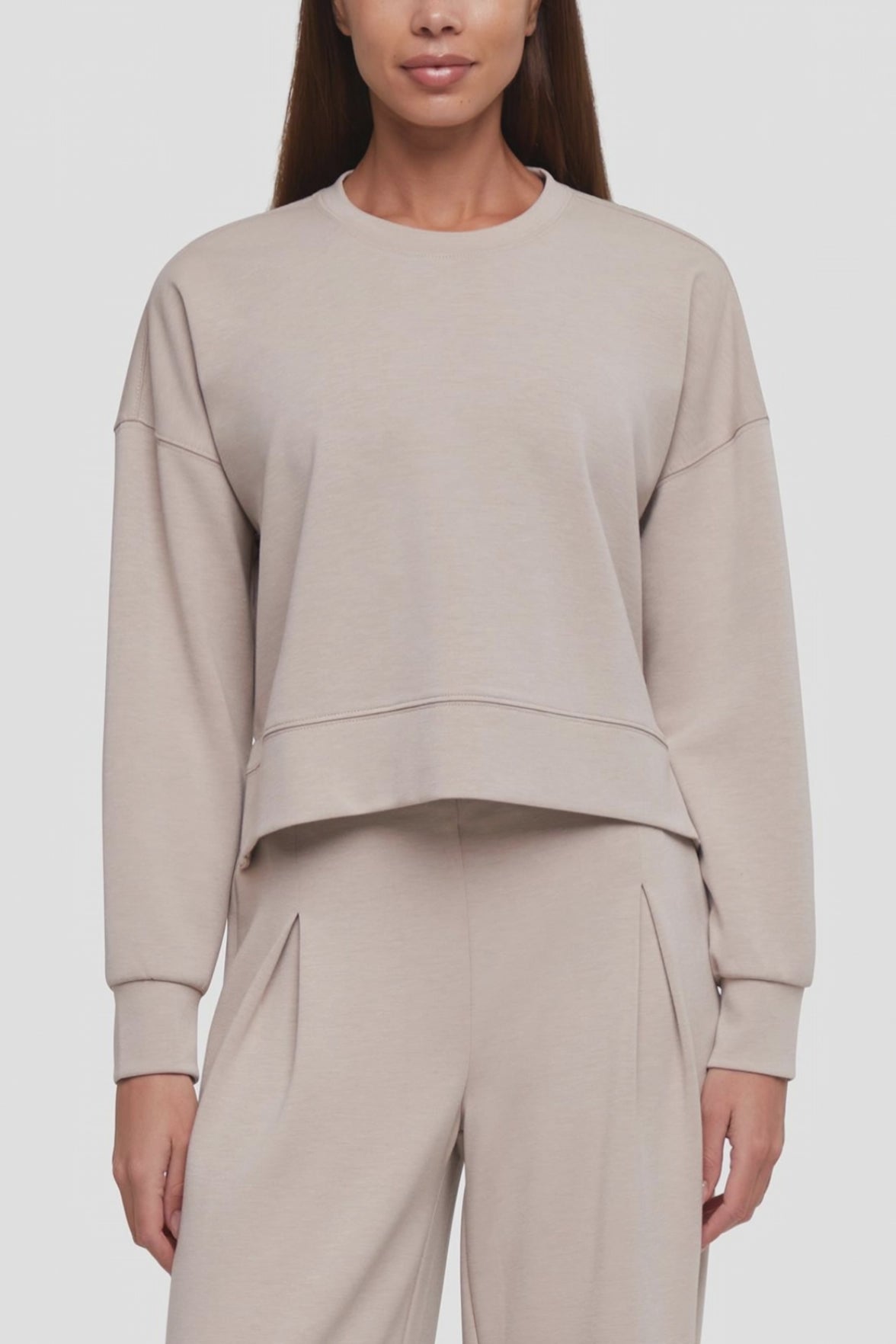 Video of a woman wearing a light beige cropped crewneck sweatshirt and matching wide-leg sweatpants against a plain light gray studio background. #color_atmosphere
