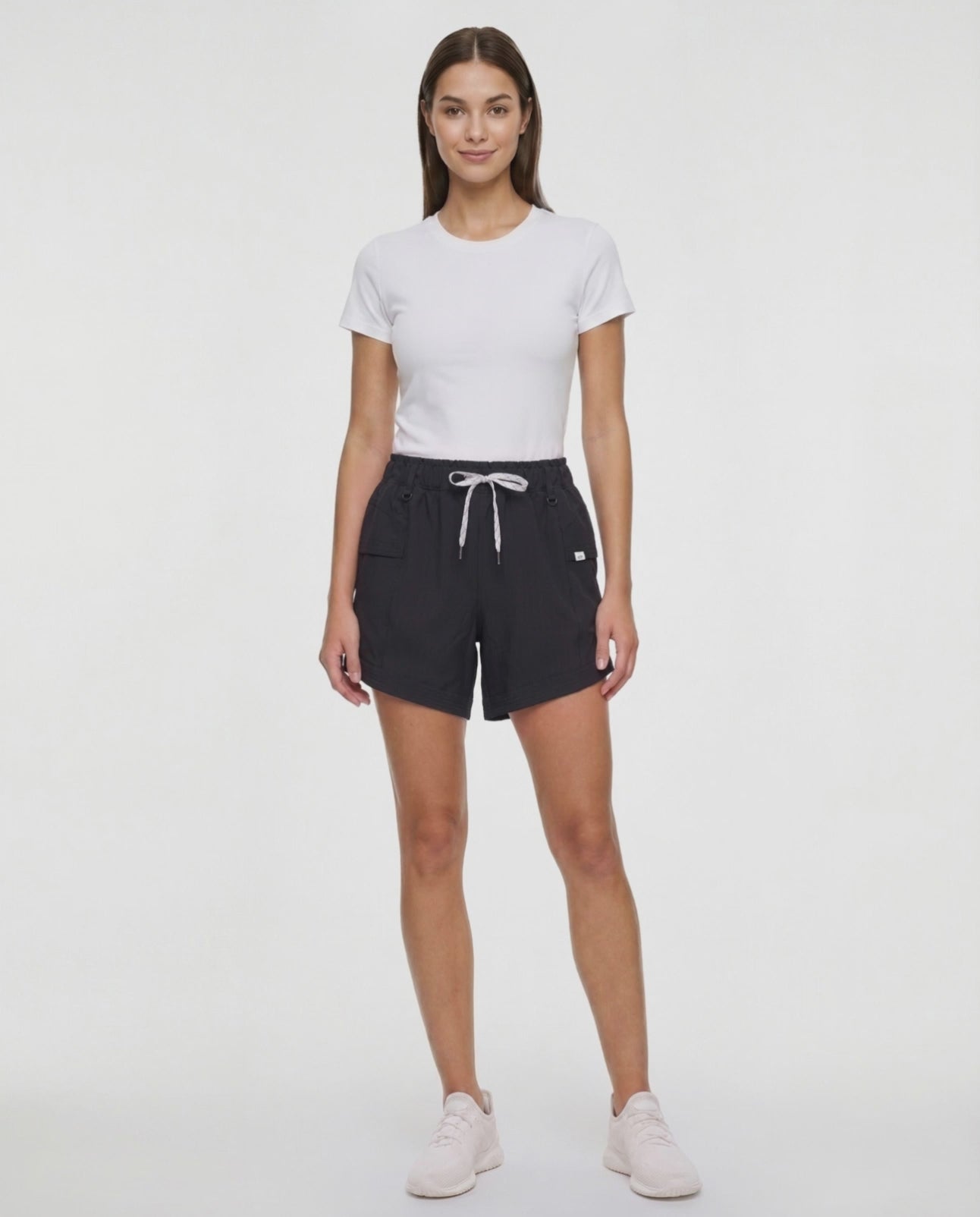 Video view of woman wearing black shorts with white drawstring waist and side pocket and white sneakers on a white background. 