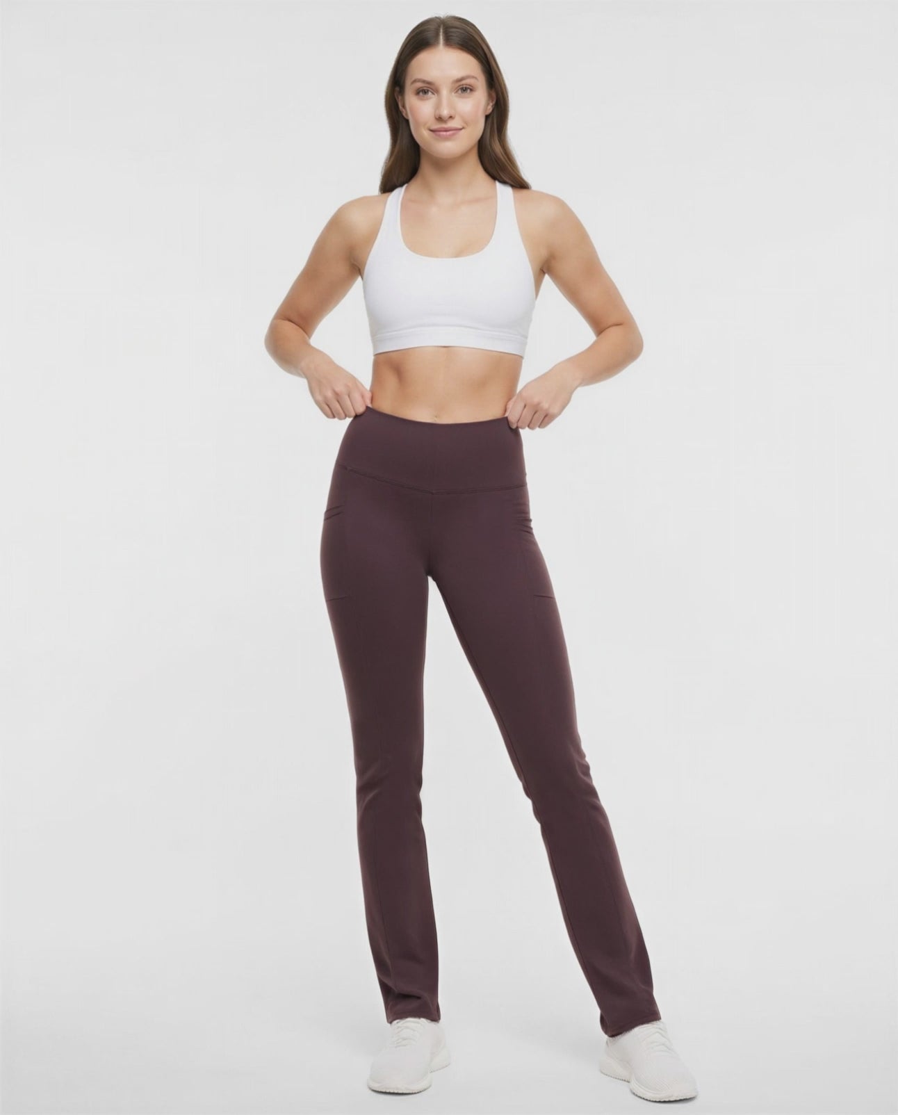 Video view of woman wearing brown yoga pants with a plain background. 