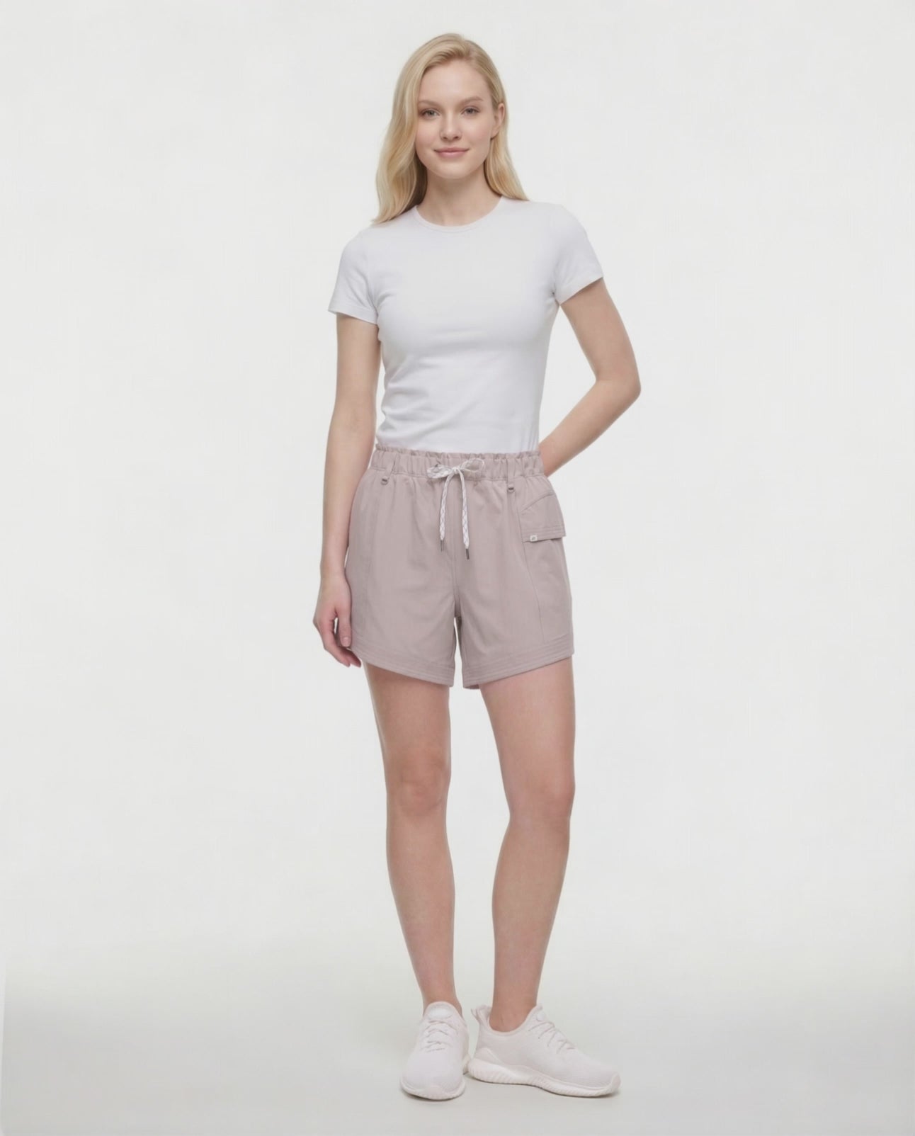Video view of woman wearing beige shorts with white drawstring waist and side pocket and white sneakers on a white background. 