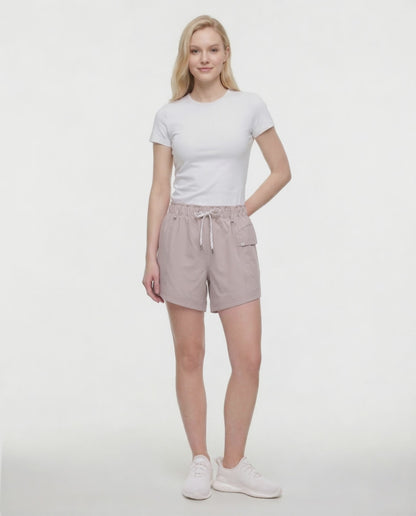 Video view of woman wearing beige shorts with white drawstring waist and side pocket and white sneakers on a white background. 