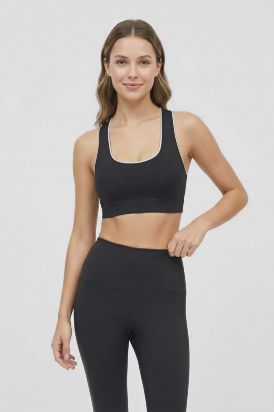Video view of woman wearing a black sports bra with white trim and black leggings on a white background. #color_black