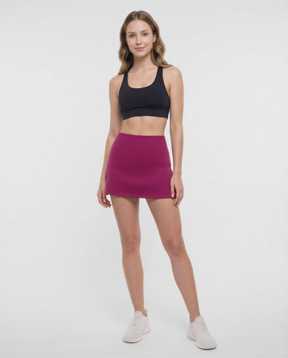 Video view of woman wearing a magenta skort and black sport bra on a white background. 