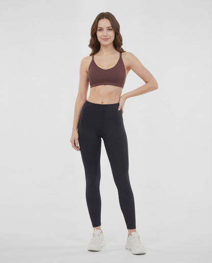 Video view of woman wearing a brown sports bra and black leggings on a white background. 