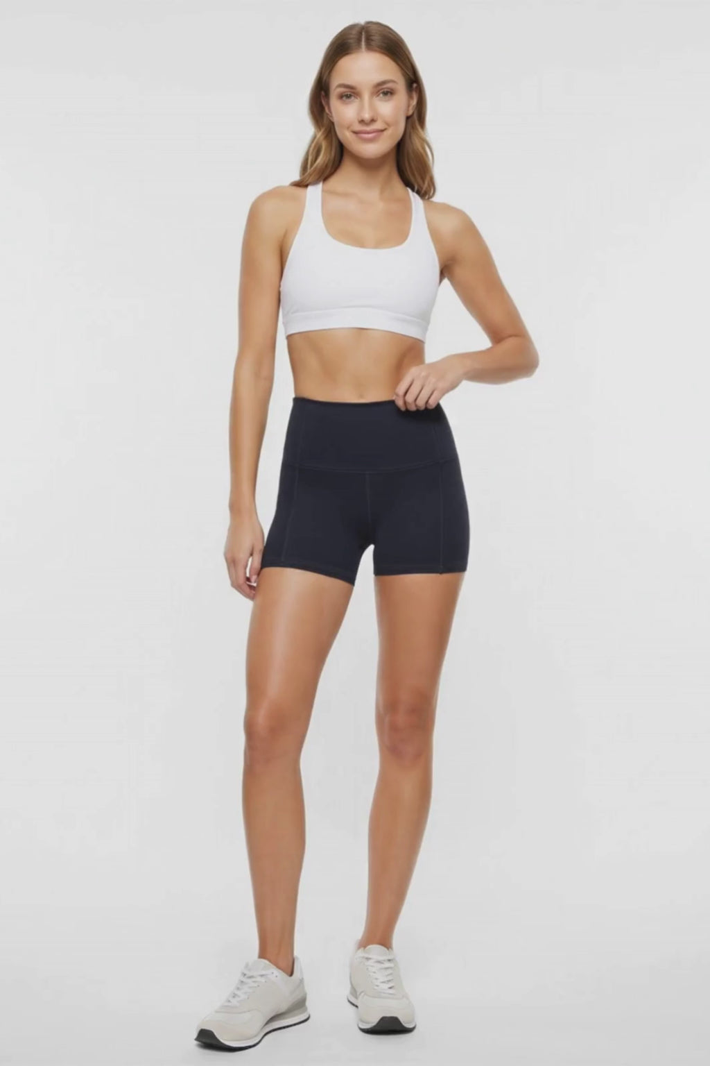 Video view of woman wearing black athletic shorts, white sports bra and white sneakers on a light background. #color_black