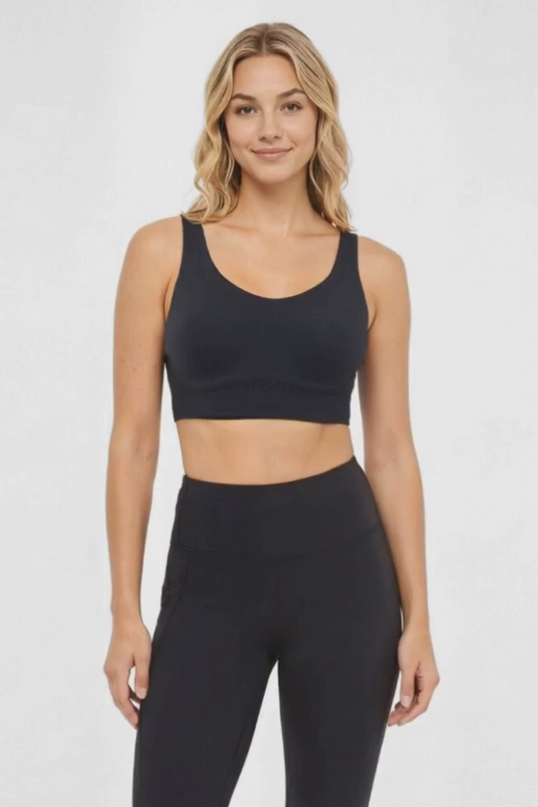 Video view of woman wearing a black sports bra and matching black leggings on a white background. 
