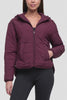 Video of a woman wearing a cropped, quilted puffer jacket in deep burgundy with a front zipper, hood, and zippered pockets, paired with black leggings, against a light gray studio background. #color_winetasting