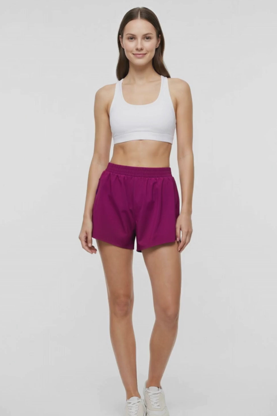 Video view of woman wearing magenta shorts and white bra on a white background. 