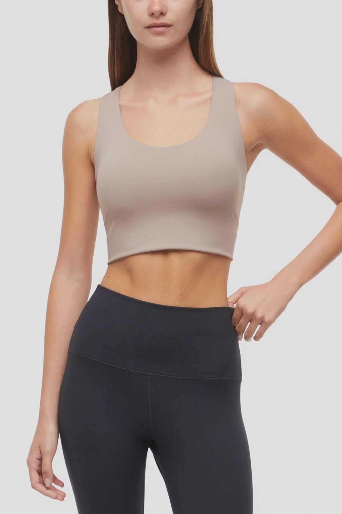 Video view of woman wearing a beige sports bra and black leggings on a white background. 