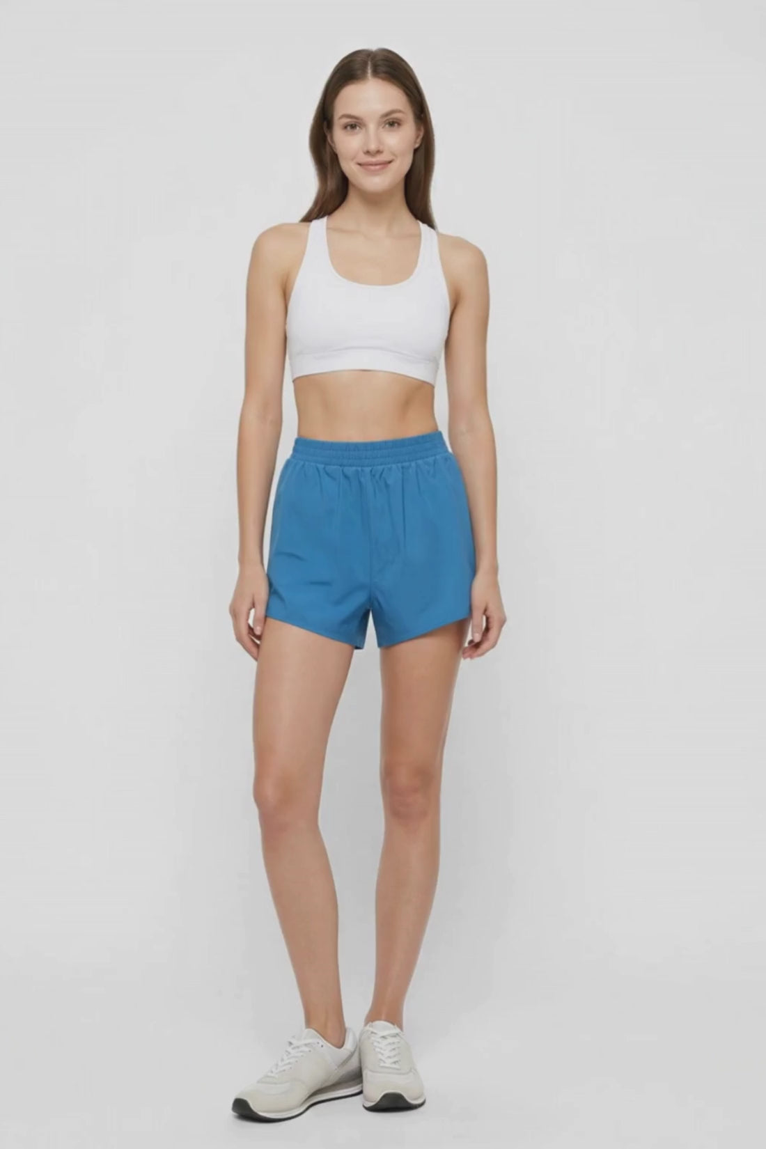 Video view of woman wearing blue shorts and white sport bra on a white background. 