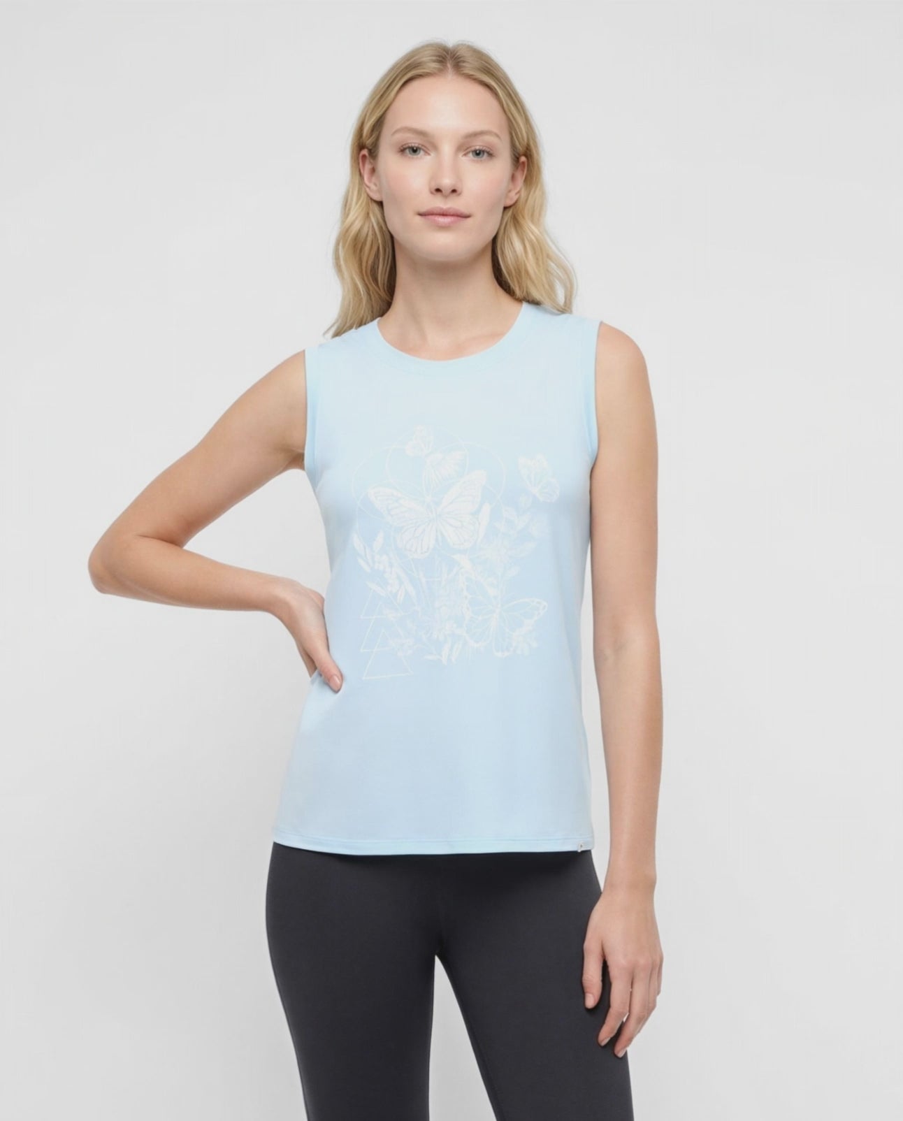 Video view of woman wearing a light blue sleeveless top with white butterflies design on a plain background. 